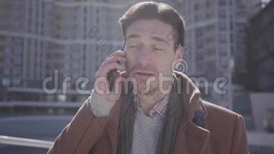 身着棕色外套的英俊自信男子站在城市街道上用手机交谈的肖像。 城市景观